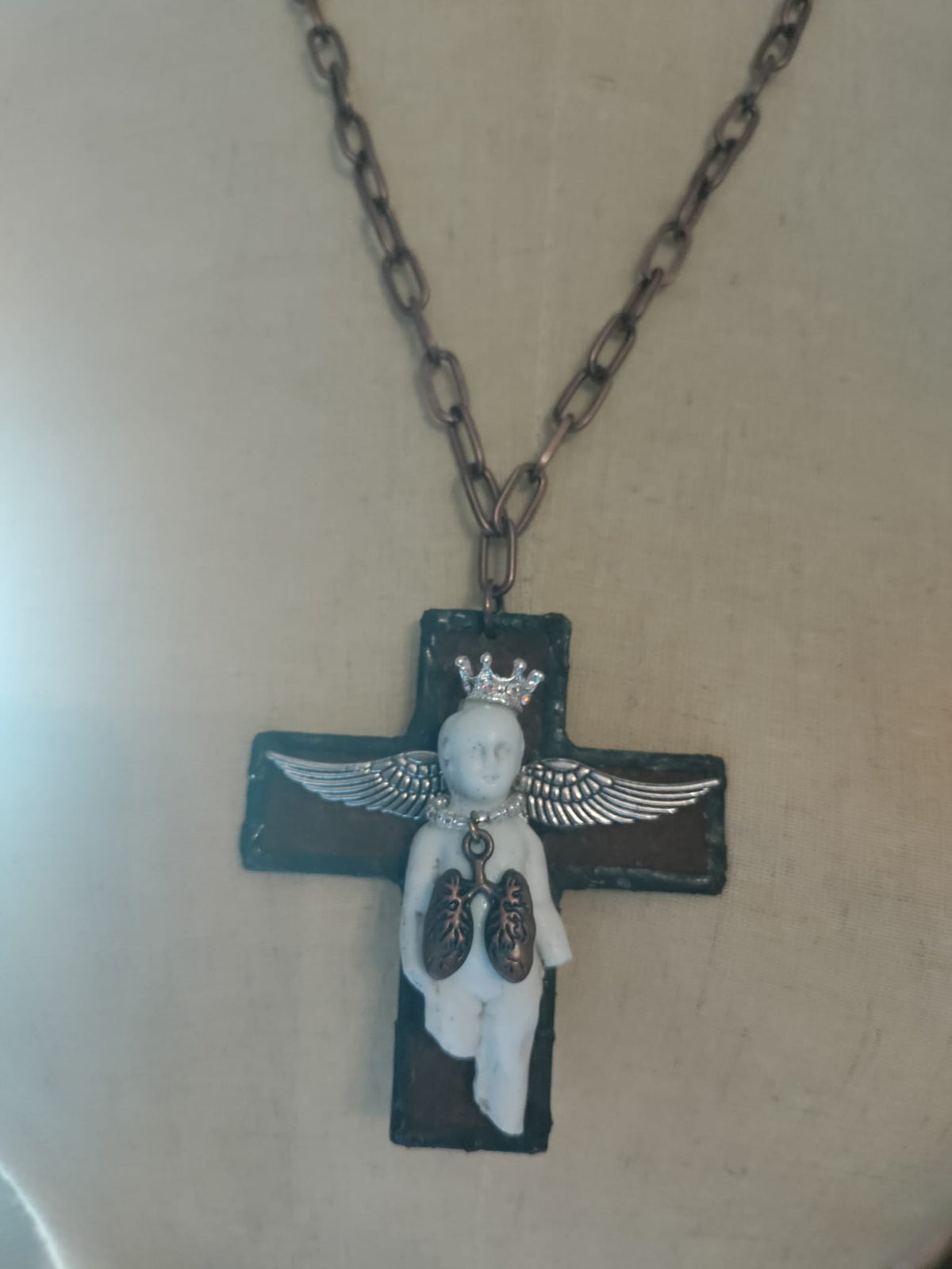 Close-up of Charles' Last Breath pendant, bisque doll figure with silver rhinestone crown, wings, and copper lungs charm on a black cross