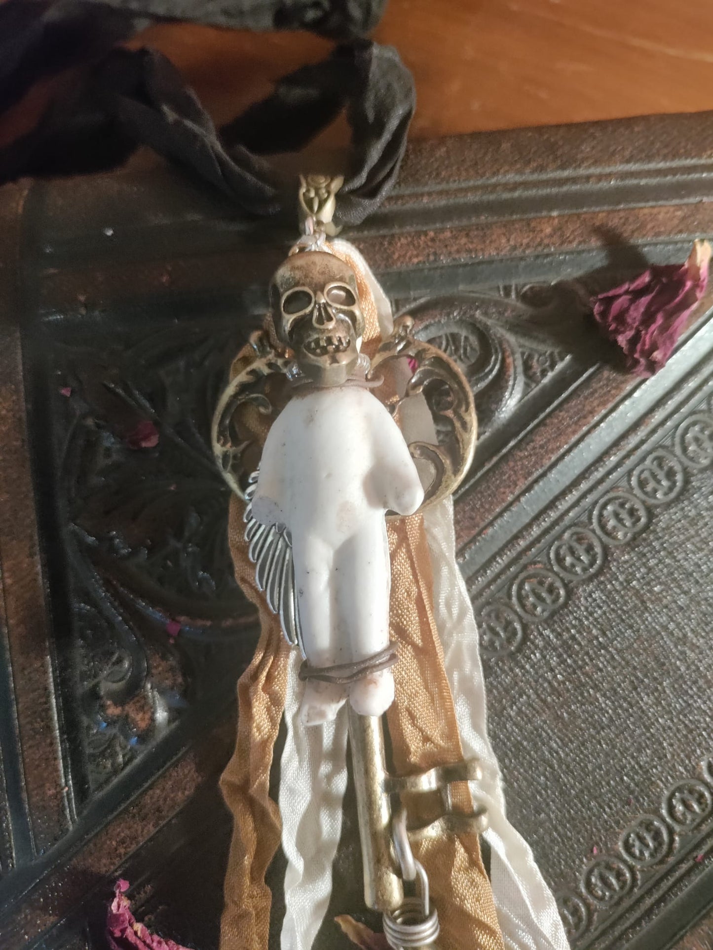 Skeleton Key Frozen Charles pendant close-up, antique bisque doll on a bronze skull and wing mount above a brass skeleton key, resting on an ornate leather book