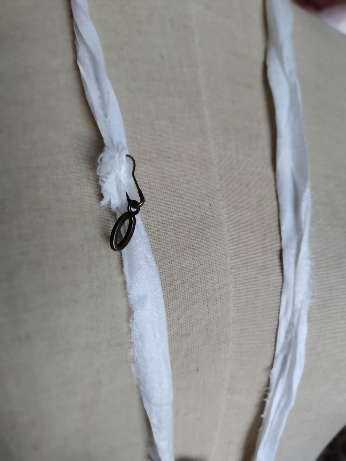 Close-up of Cypher in the Snow necklace clasp, bronze hook and ring fastening on the ivory silk ribbon