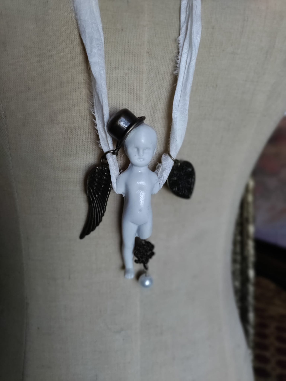 Cypher in the Snow pendant on mannequin, front view of bisque doll figure with top hat, bronze angel wing, and filigree heart charm
