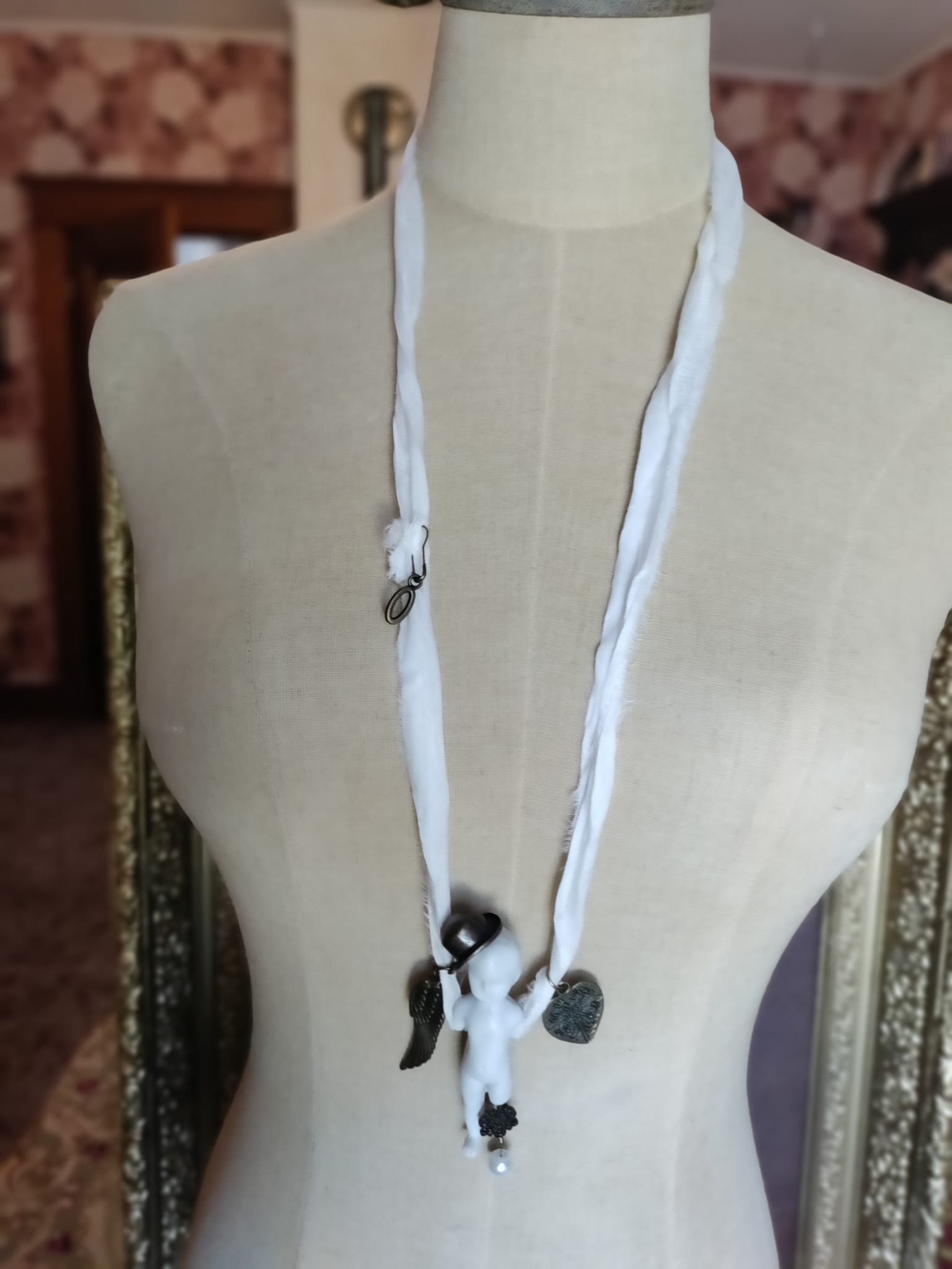 Cypher in the Snow necklace on mannequin, ivory silk ribbon necklace with bisque doll pendant in a top hat and bronze charms