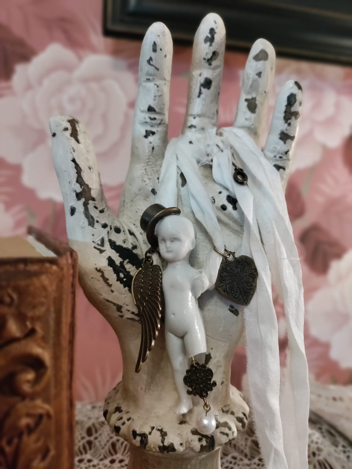 Cypher in the Snow necklace displayed on a plaster hand form, bisque doll figure in a small black top hat with bronze wing and filigree heart charms on ivory silk ribbons