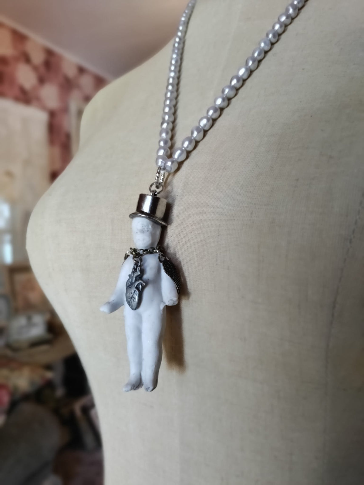 Charlie's Broken Heart necklace on mannequin, side view of pearl bead chain and bisque doll pendant with top hat and heart charm