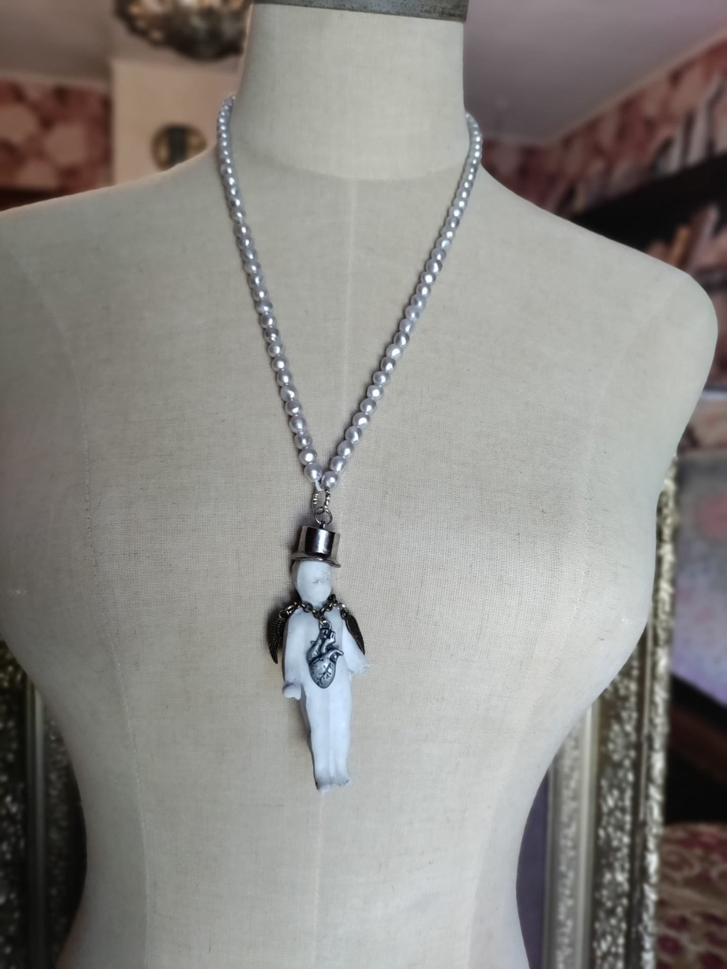 Charlie's Broken Heart necklace on mannequin, long pearl bead chain with bisque doll pendant in a silver top hat and silver angel wings