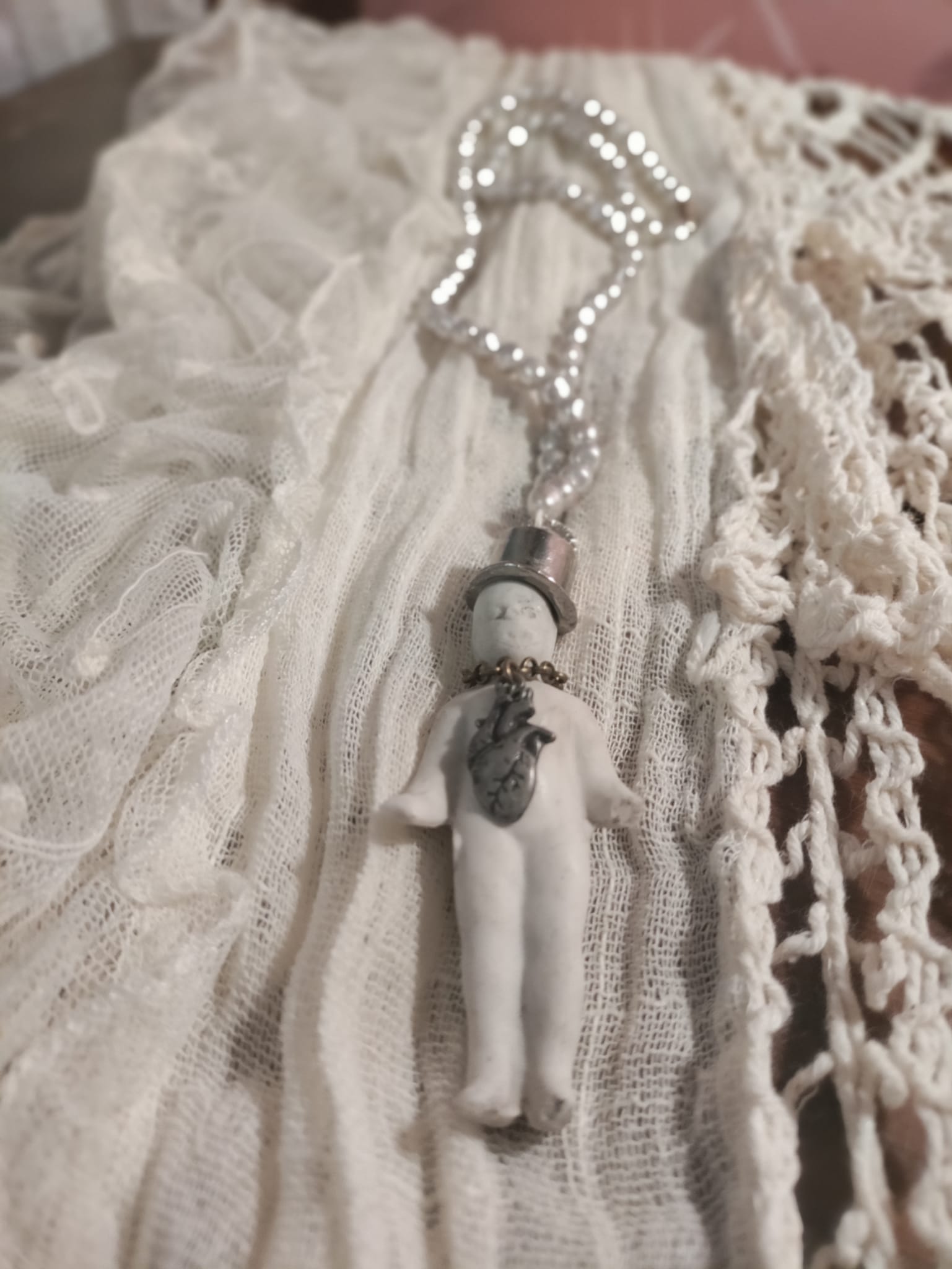 Close-up of Charlie's Broken Heart pendant resting on antique lace, bisque doll in a silver top hat with pewter anatomical heart charm