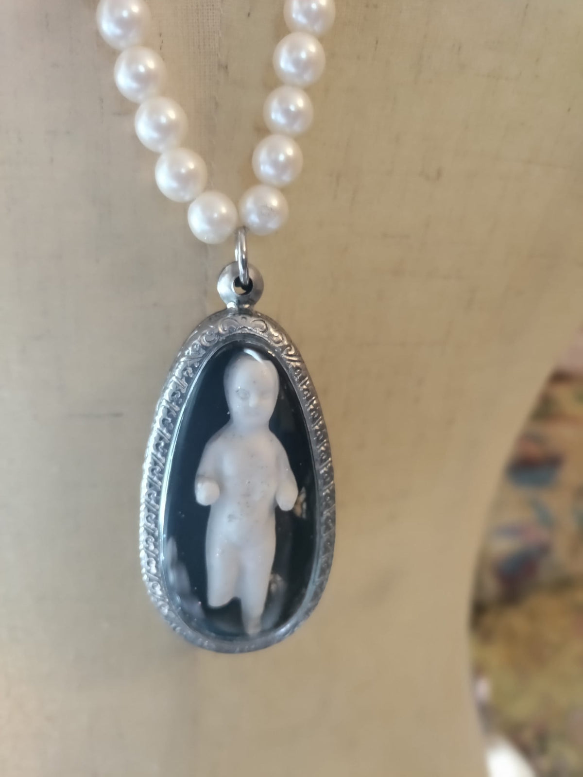Close-up of Reliquary Frozen Charles pendant, antique bisque doll fragment sealed in an ornate oval silver bezel with black background