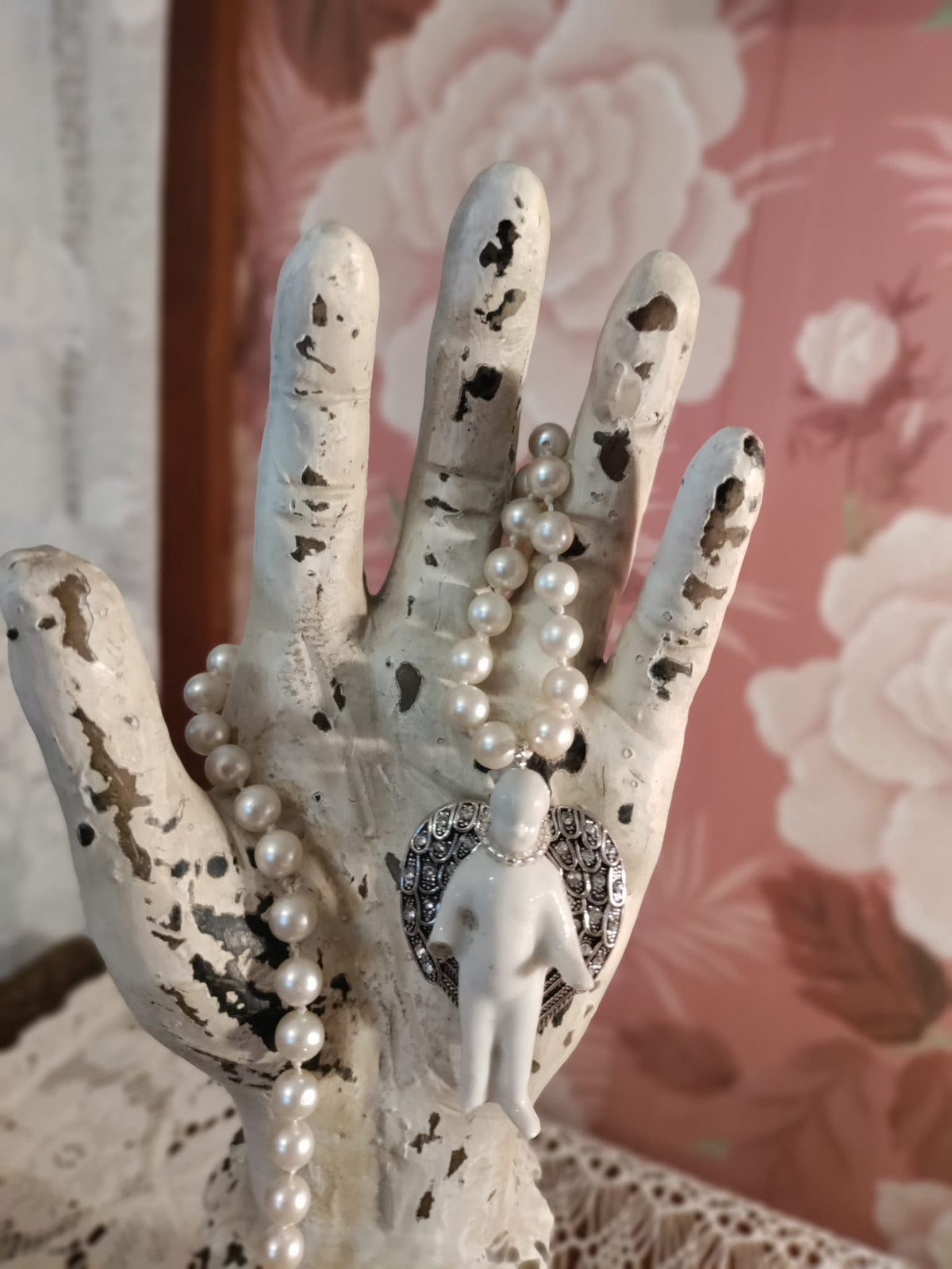 Close-up of the Frozen Charlotte bisque doll pendant with silver rhinestone pavé angel wings, hanging from knotted glass pearls on a display hand