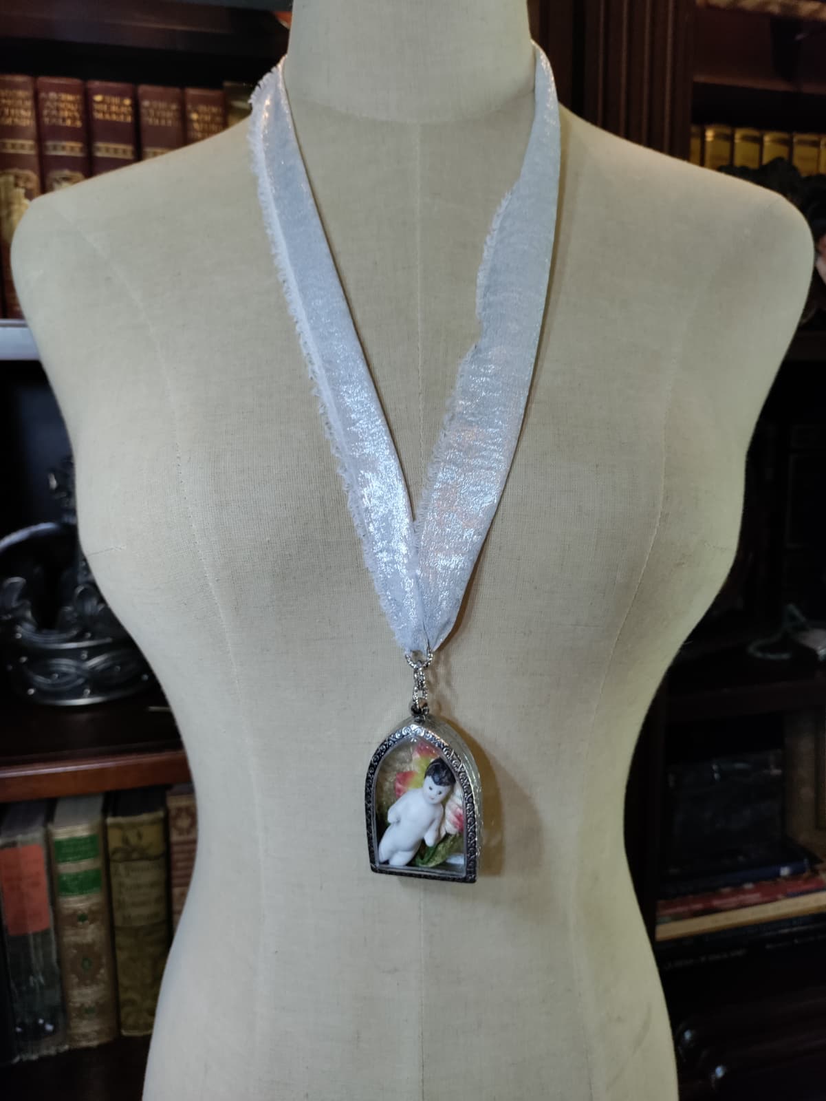 Frozen Charlotte necklace with antique bisque doll in a silver arched frame surrounded by pink and red flowers, worn on a shimmering silver ribbon