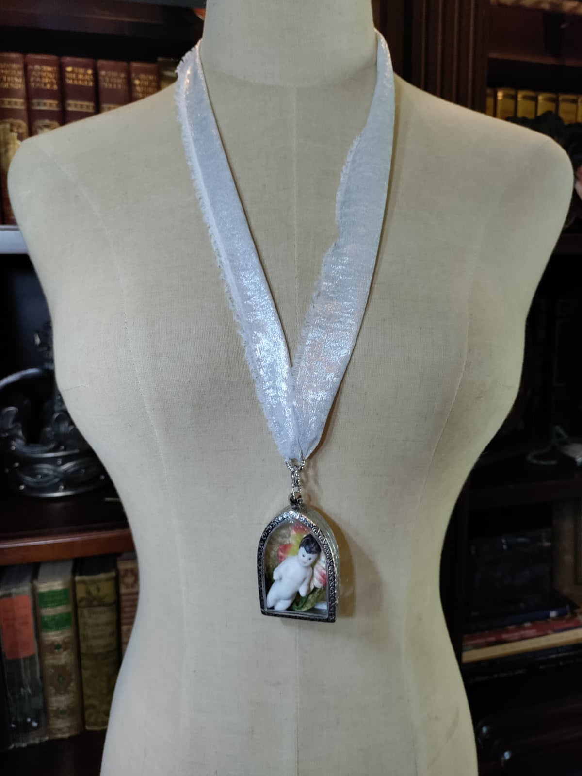 Frozen Charlotte necklace with antique bisque doll in a silver arched frame surrounded by pink and red flowers, worn on a shimmering silver ribbon