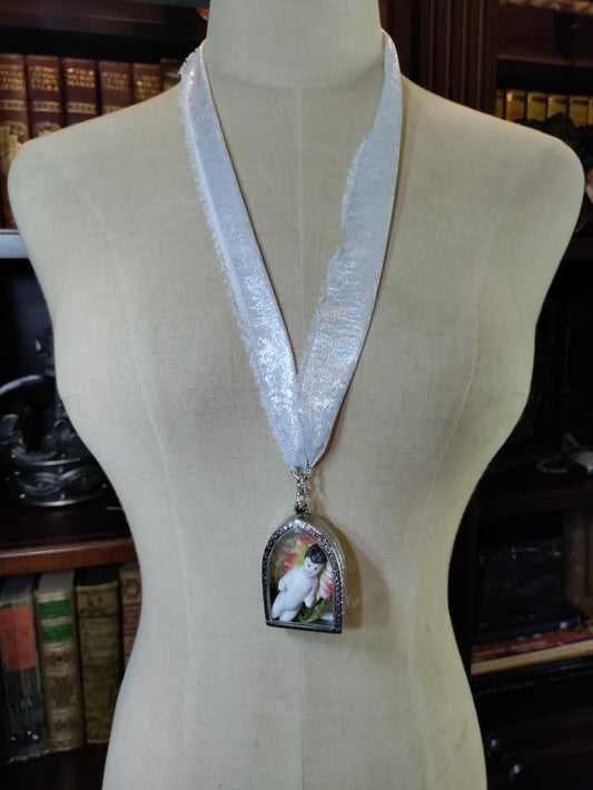 Frozen Charlotte necklace with antique bisque doll in a silver arched frame surrounded by pink and red flowers, worn on a shimmering silver ribbon