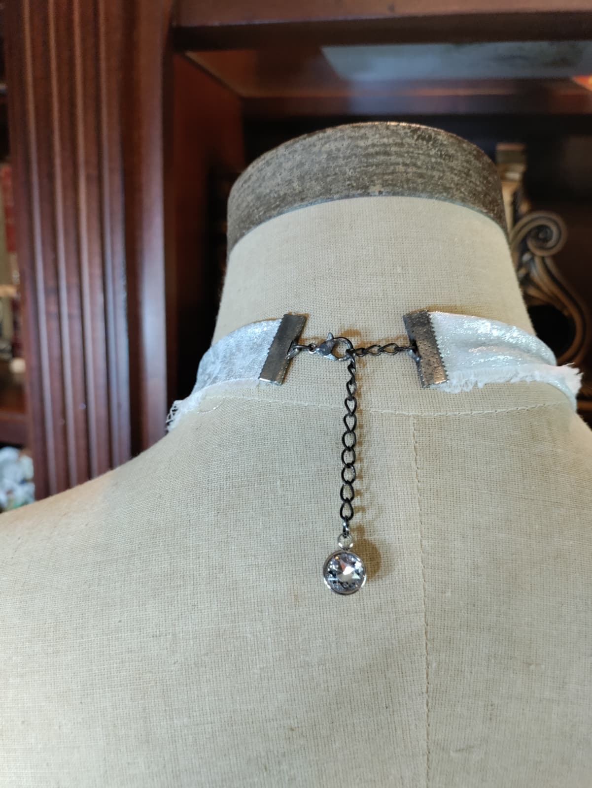 Close-up of Frozen Charlotte necklace pendant resting on an antique book, surrounded by dried rose petals, greenery, and lace