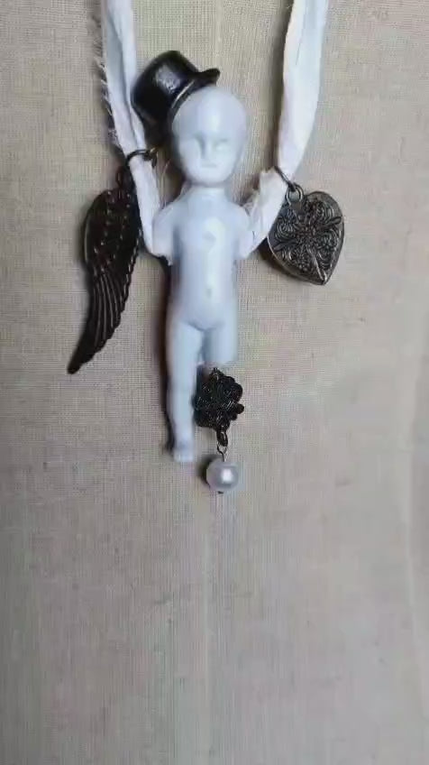 Video of the Cypher in the Snow necklace showing the bisque doll pendant with top hat, bronze wing, and heart charm in motion